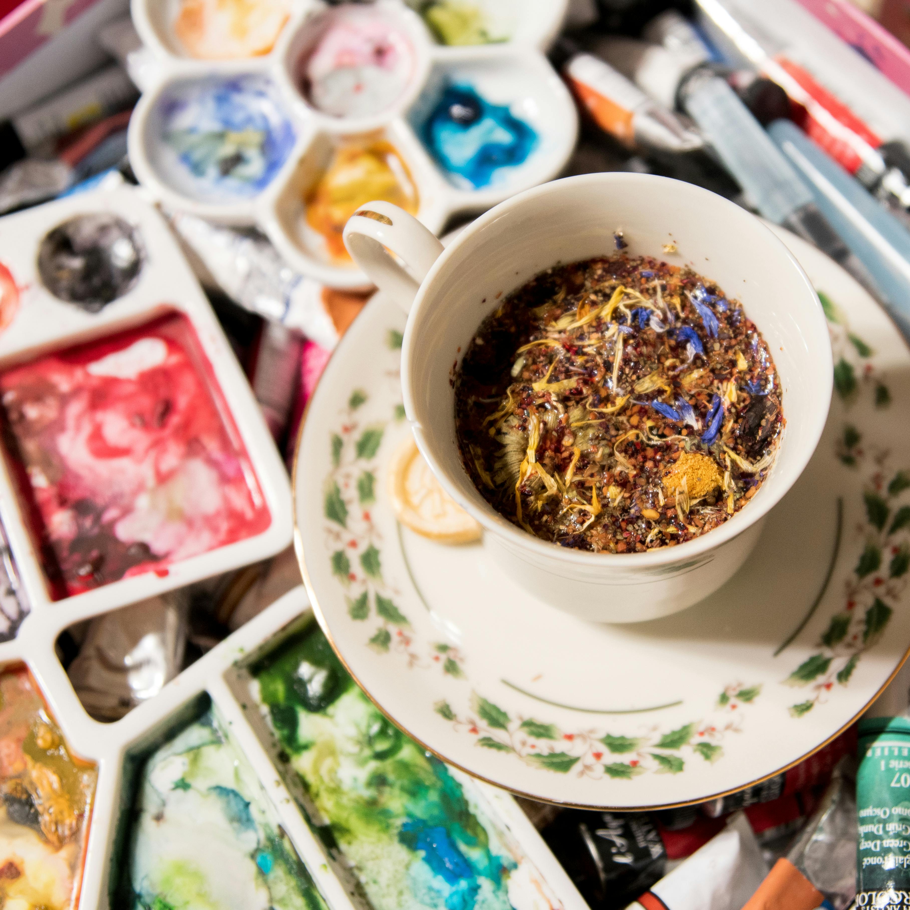 A vibrant herbal tea cup surrounded by colorful watercolor palettes, blending art and relaxation.