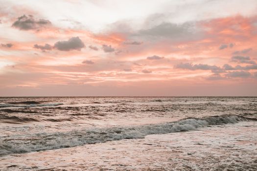 Capture the serene beauty of waves and a vibrant pink sunset over the ocean.