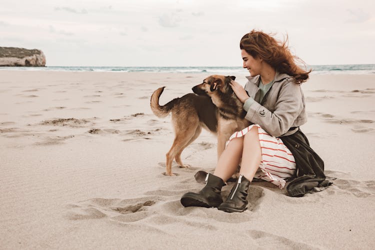 Happy Woman With Dog Sitting On Sand Beach