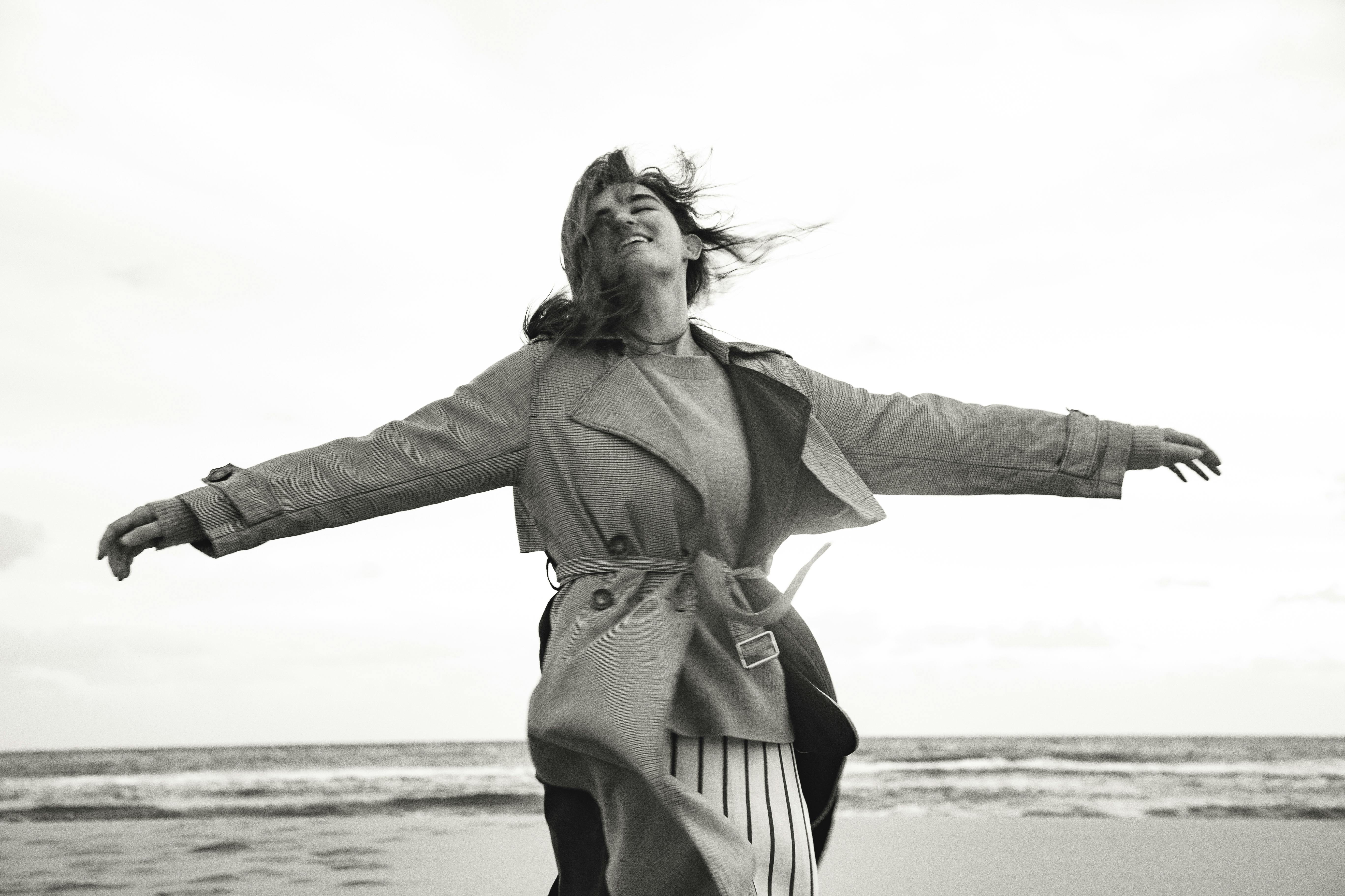 黑白摄影中，穿着外套的女人在多风的海滩上感受自由