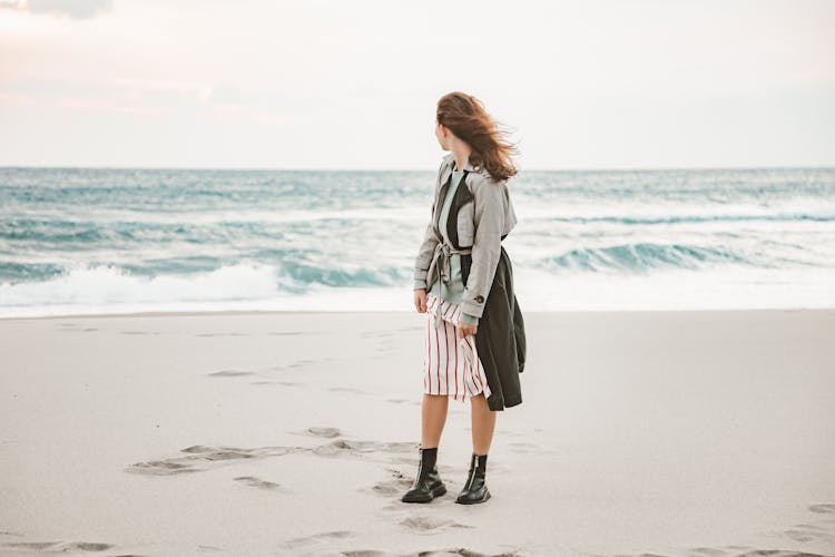 A Woman Wearing Boots And A Coat At The Beach 