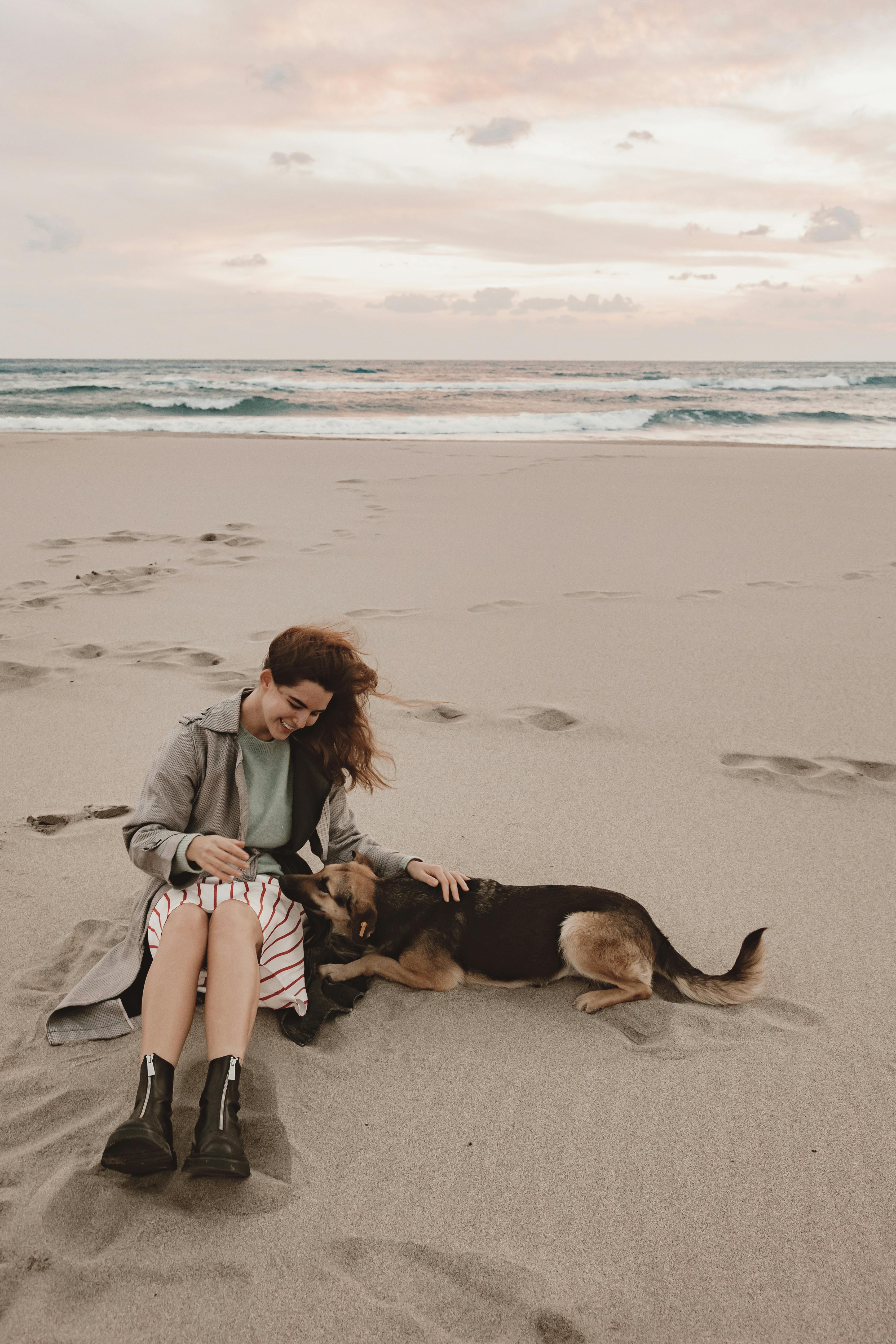 Woman sitting with her dog on a serene beach, creating a peaceful seaside moment.