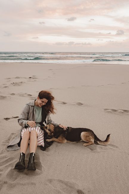 Woman sitting with her dog on a serene beach, creating a peaceful seaside moment.