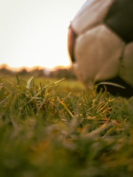 Artistic close-up of a soccer ball resting on grass with warm sunset lighting, ideal for sports and leisure themes.