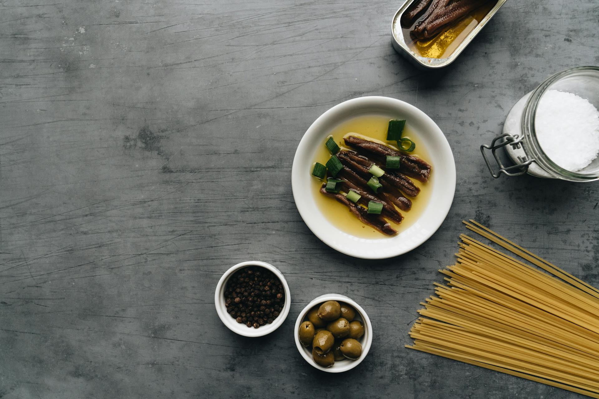 Delicious Anchovies with Oil and Onion Leeks Beside a Bowl of Pepper and Olives