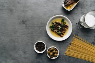 Delicious Anchovies with Oil and Onion Leeks Beside a Bowl of Pepper and Olives