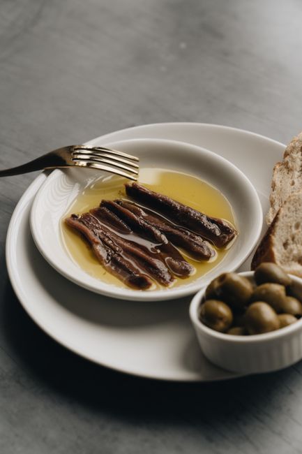 A close-up of anchovies in oil with olives and bread on a plate, perfect for appetizer inspiration.