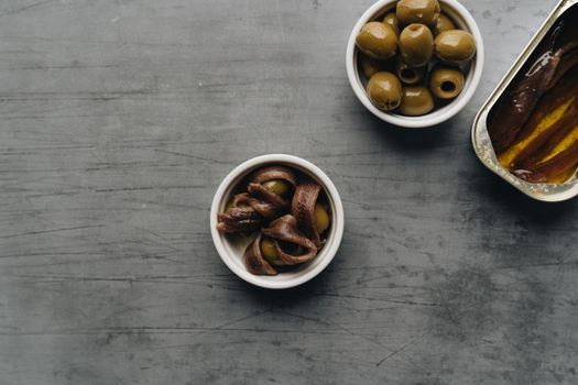Close-up of fresh anchovies and green olives in bowls on a rustic table setting, showcasing simple gourmet ingredients.