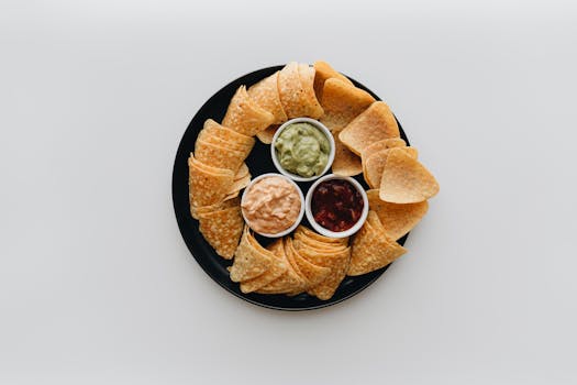 Top view of tortilla chips with guacamole, salsa, and cheese dips on a black plate. Perfect for Mexican cuisine lovers.