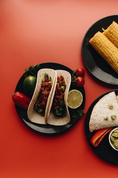 A vibrant food photo showcasing Mexican tacos and fresh vegetables on a red background.