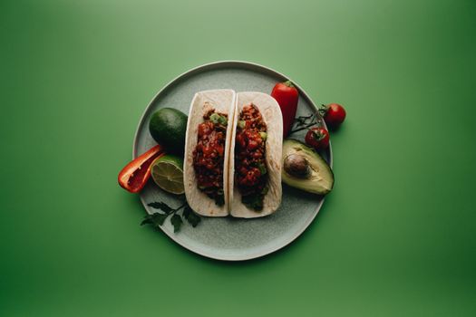 Photo by alleksana Top view of tasty Mexican tacos with fresh ingredients on a vibrant green background.