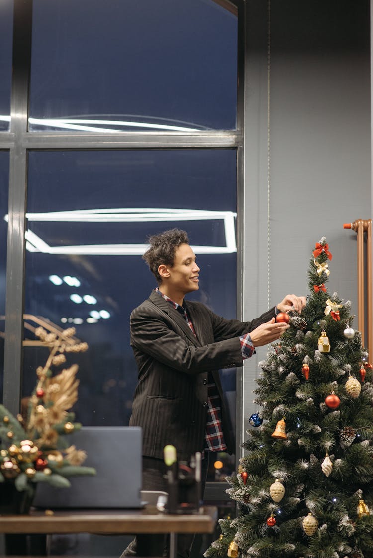 A Man In Black Suit Putting Ornaments On The Christmas Tree