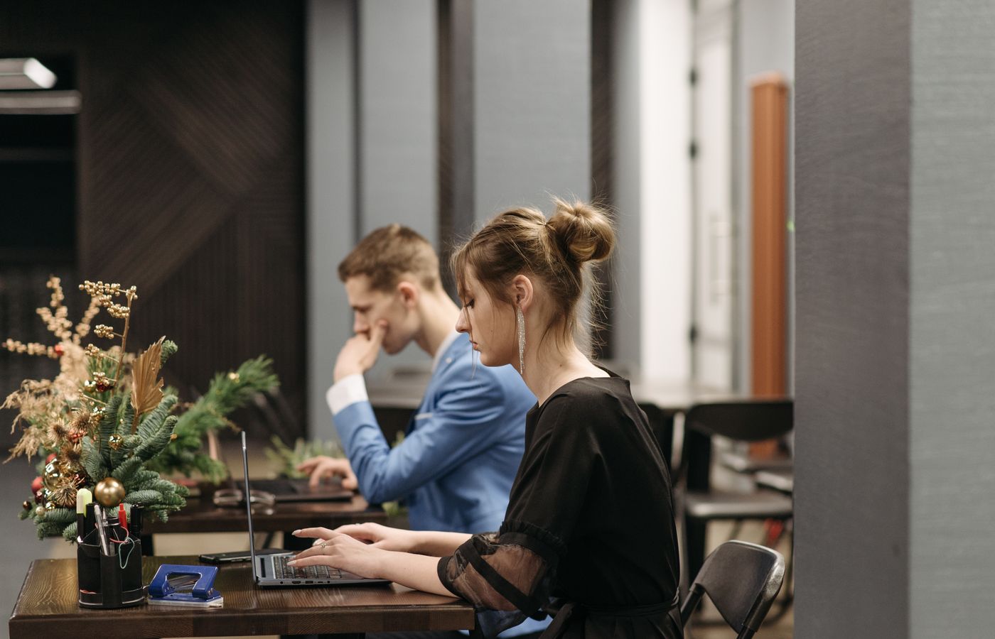 Two adults working on laptops in a Christmas-themed office, maintaining focus and productivity.