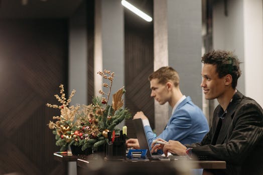 Two men working on laptops in a festively decorated office during Christmas.