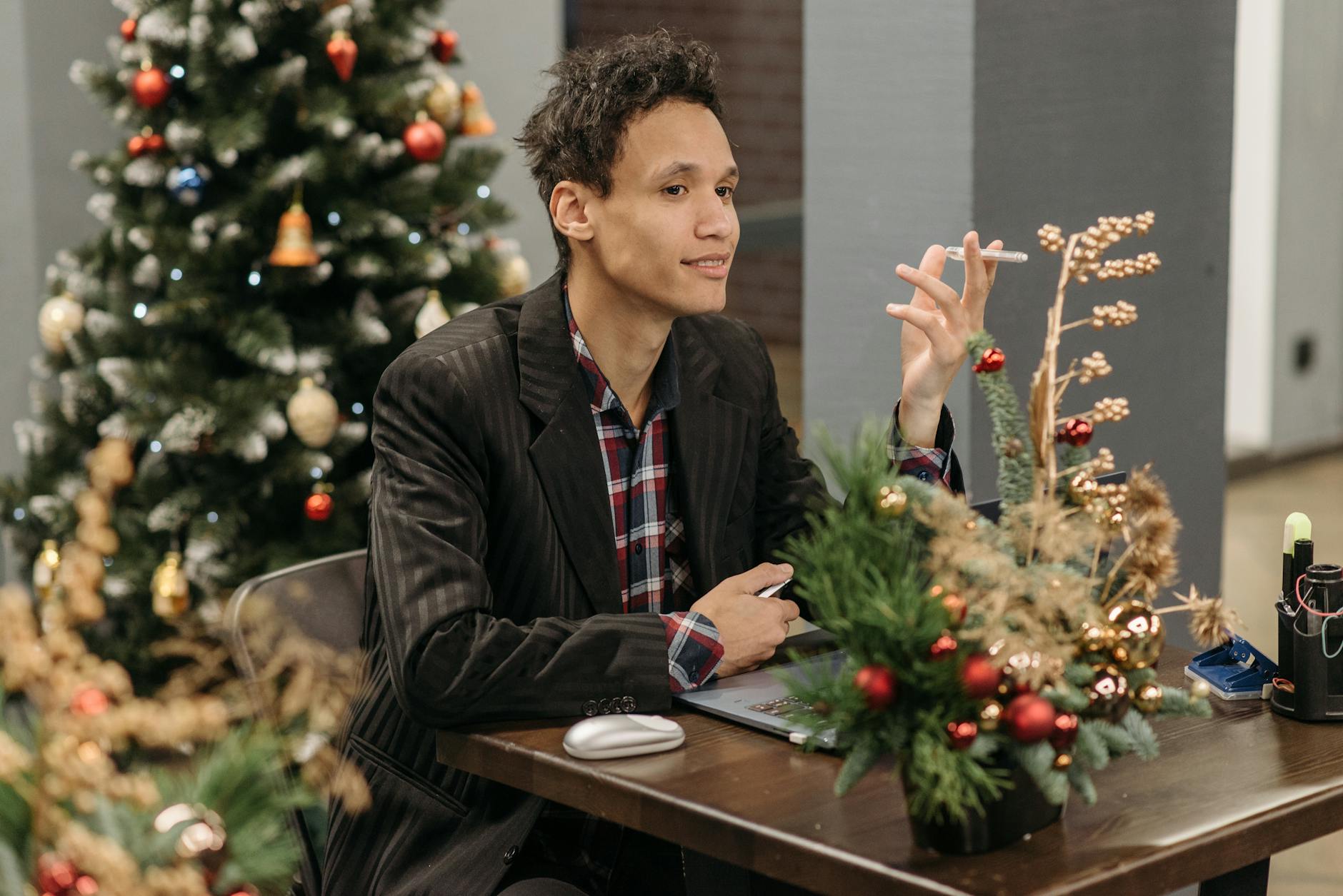 Man sitting at office desk, surrounded by festive Christmas decorations and a tree.