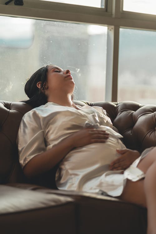 Free Serene pregnant woman lying on cozy sofa with eyes closed Stock Photo