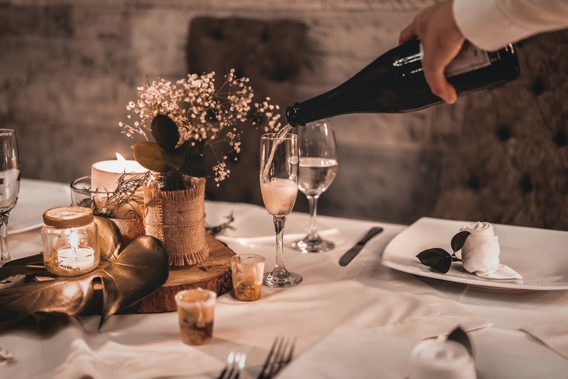 Free Crop anonymous waiter pouring sparkling champagne into wineglass placed on table with tableware and burning candles in restaurant Stock Photo