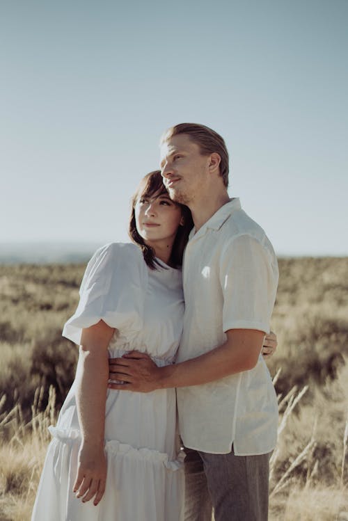 Young romantic couple hugging in rural field and looking away in sunny summer day