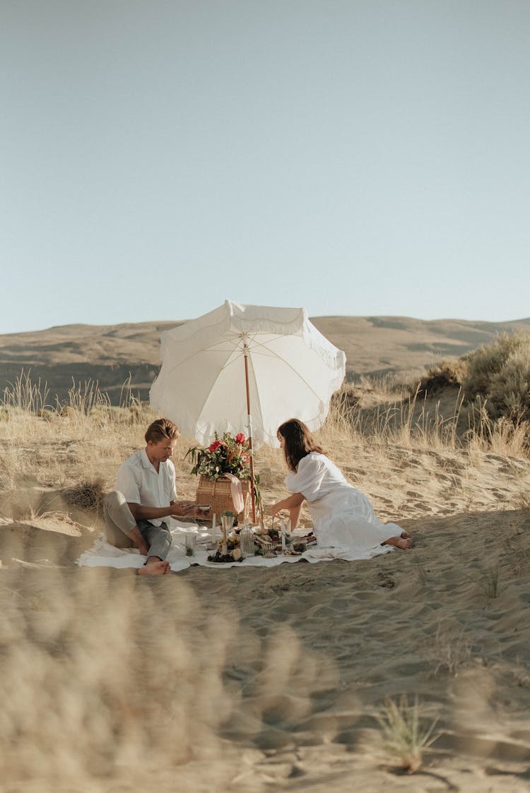 Man And Woman Resting On Sandy Beach And Having Picnic