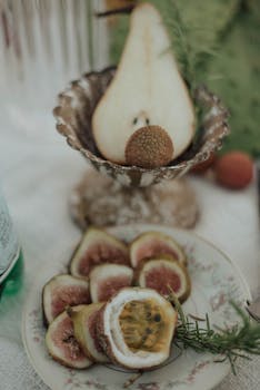 High angle of served table with cut figs and rosemary twig on plate and half of pear in silver vase