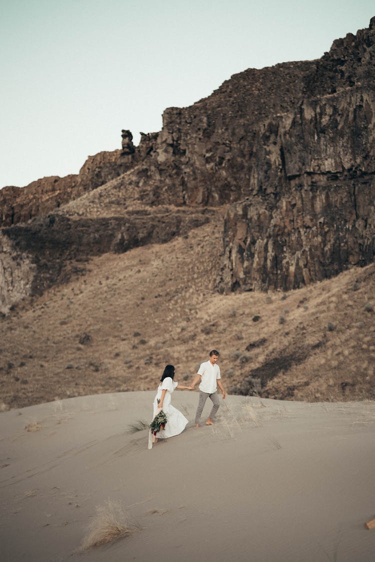 Anonymous Couple On Sandy Coast Near Hills With Grass