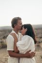 Side view of tender boyfriend kissing forehead of beloved girlfriend while cuddling on grassy meadow in nature during romantic date