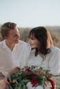 Happy newlyweds with flowers sitting in nature