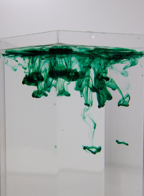 Transparent vase with green pigment fluids with spots in pure water on white background