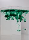 Transparent vase with green pigment fluids with spots in pure water on white background