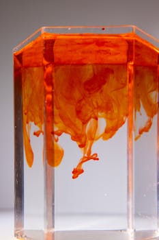 Orange ink swirls vividly in a transparent glass, showcasing fluid motion and color dynamics.