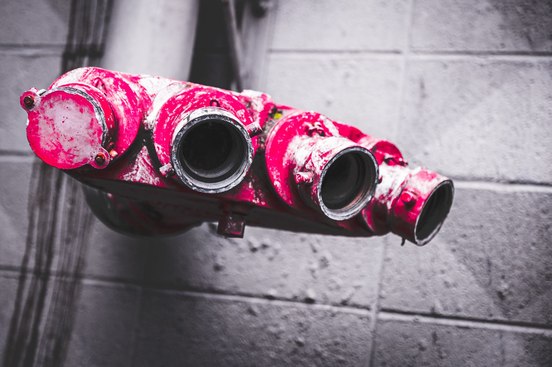 Close-up of weathered red fire hose connections against a textured brick wall, showcasing industrial decay.