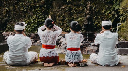 Free Four people in traditional attire praying at a Balinese temple, symbolizing cultural spirituality. Stock Photo