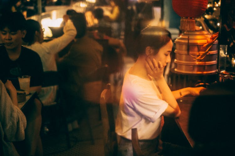 Asian Woman Resting At Bar Counter With Unrecognizable People