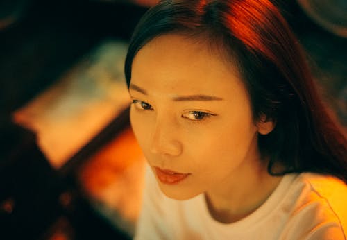 Free Crop young pleasant Asian female in white apparel looking away with deep gaze on blurred background Stock Photo