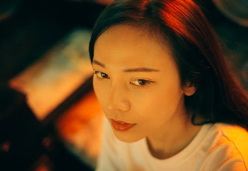 Crop young pleasant Asian female in white apparel looking away with deep gaze on blurred background