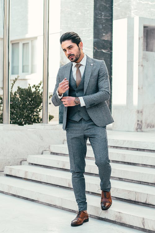 Full body of self assured young bearded male manager in formal suit walking downstairs of modern in city