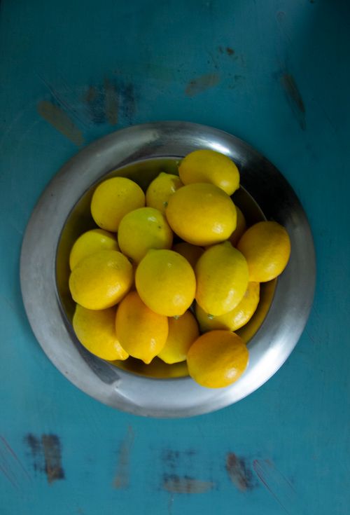 Free Top view of fresh yellow lemons in a metallic bowl placed on a vibrant blue surface. Stock Photo