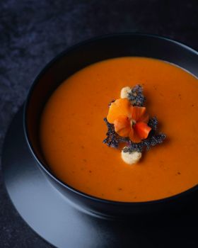 Delicious tomato soup elegantly presented with edible flower and crispy garnish.
