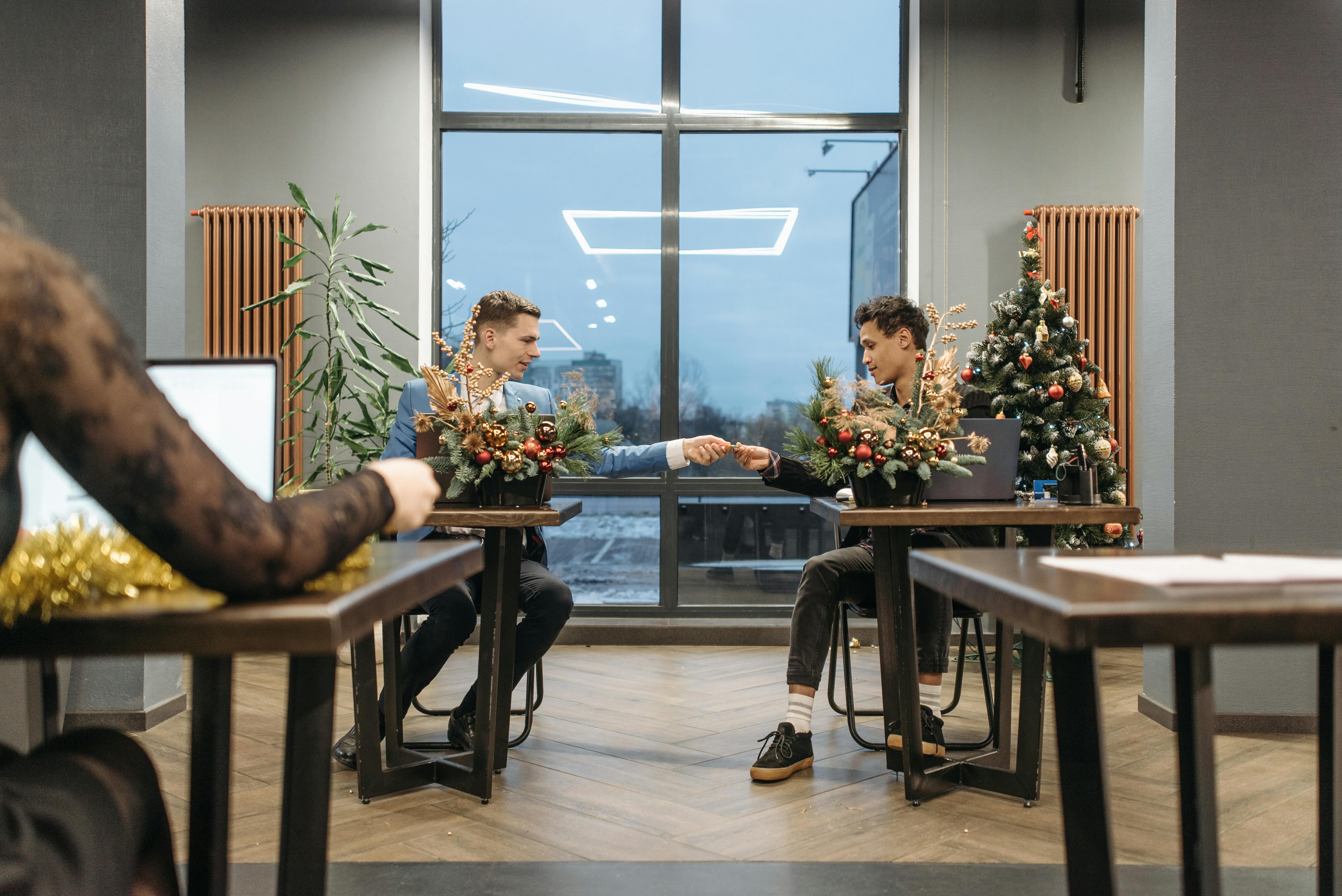 Two colleagues exchange gifts in a decorated office during Christmas season.