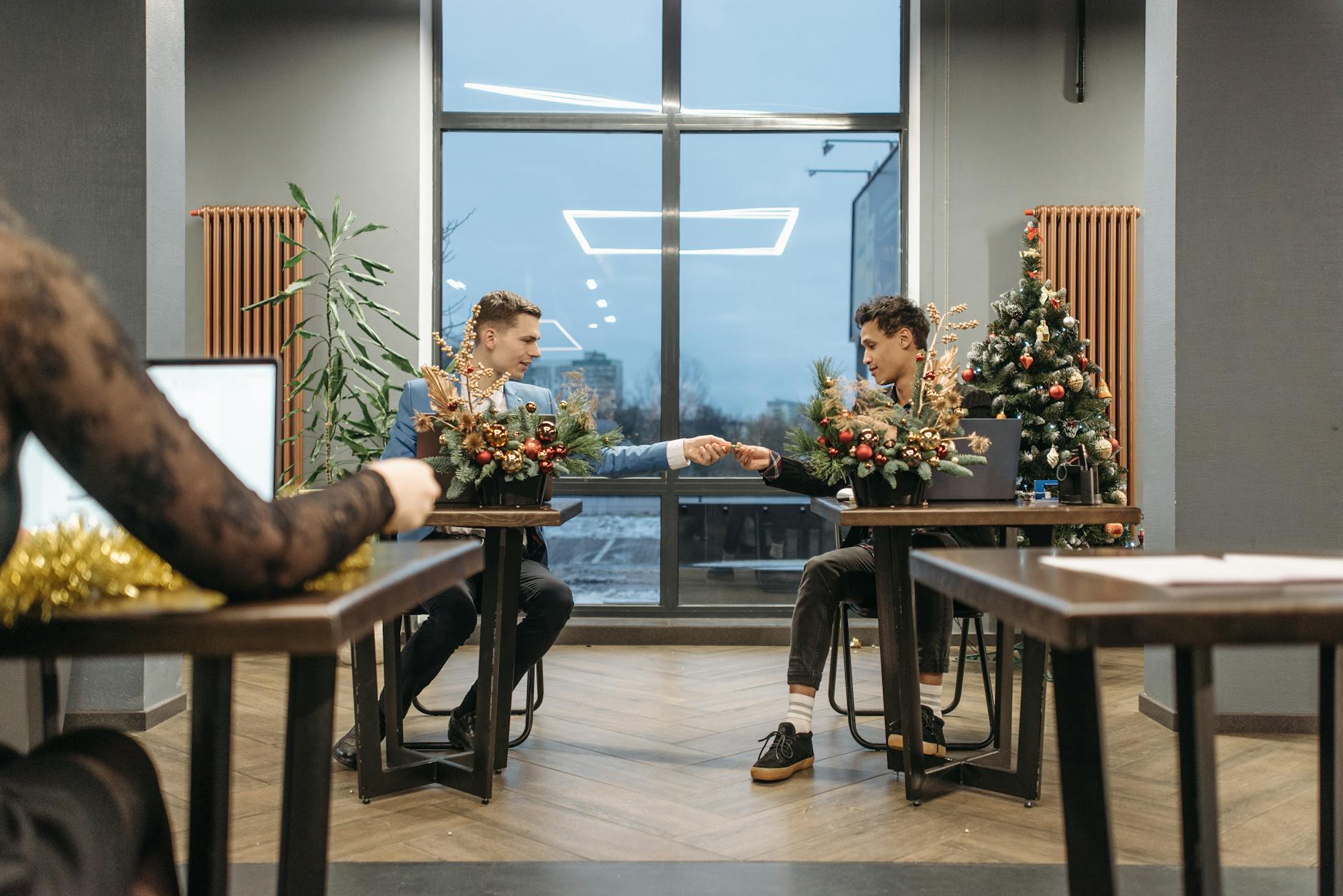 Two colleagues exchange gifts in a decorated office during Christmas season.