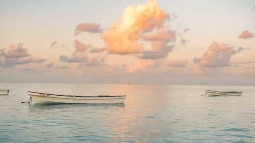 Free Tranquil sunset over a calm ocean with three boats and pastel clouds, evoking peace and serenity. Stock Photo