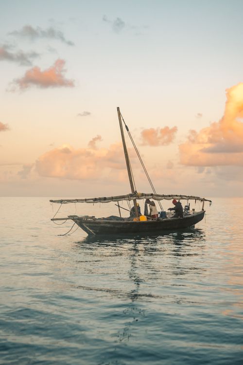 Free Fishermen on a boat at sunrise, casting nets over a calm ocean backdrop. Stock Photo