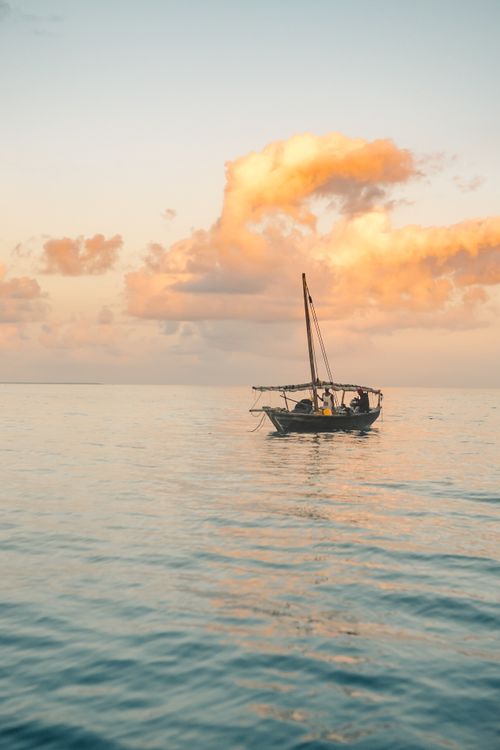 Free A lone sailboat sailing on a calm ocean during a beautiful sunset, creating a peaceful scene. Stock Photo