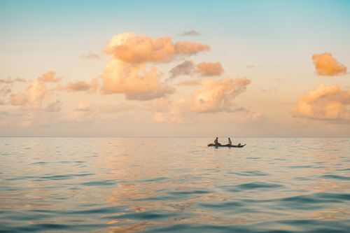 Free A tranquil scene of two people on a wooden boat at sunrise, under a vibrant cloudscape. Stock Photo