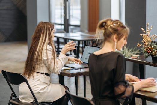 Two women working on laptops in a modern office, with focus and collaboration.