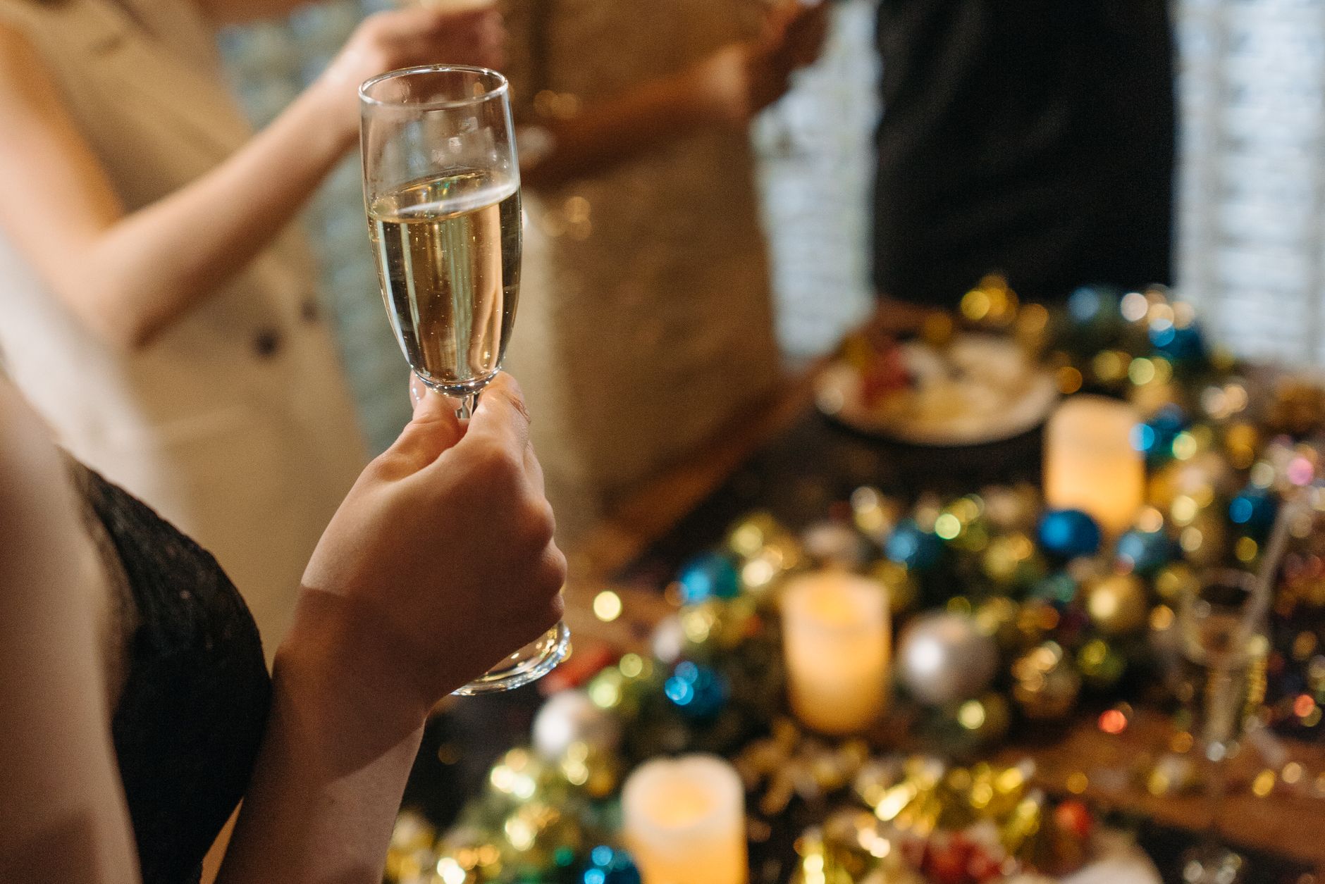 Close-up of hands holding champagne glasses at a festive gathering with candles and decor.