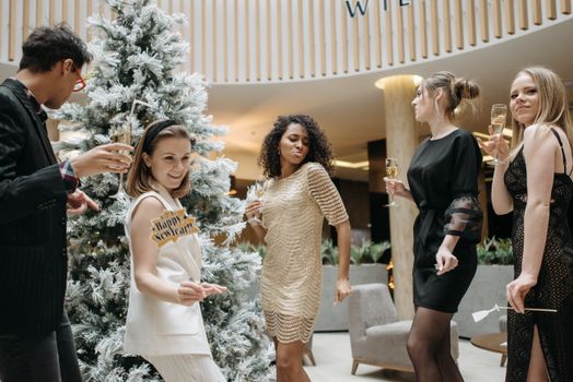 Five friends in stylish attire celebrate New Year indoors with champagne and laughter.