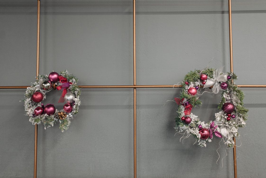 Two green Christmas wreaths with baubles hanging on a wall