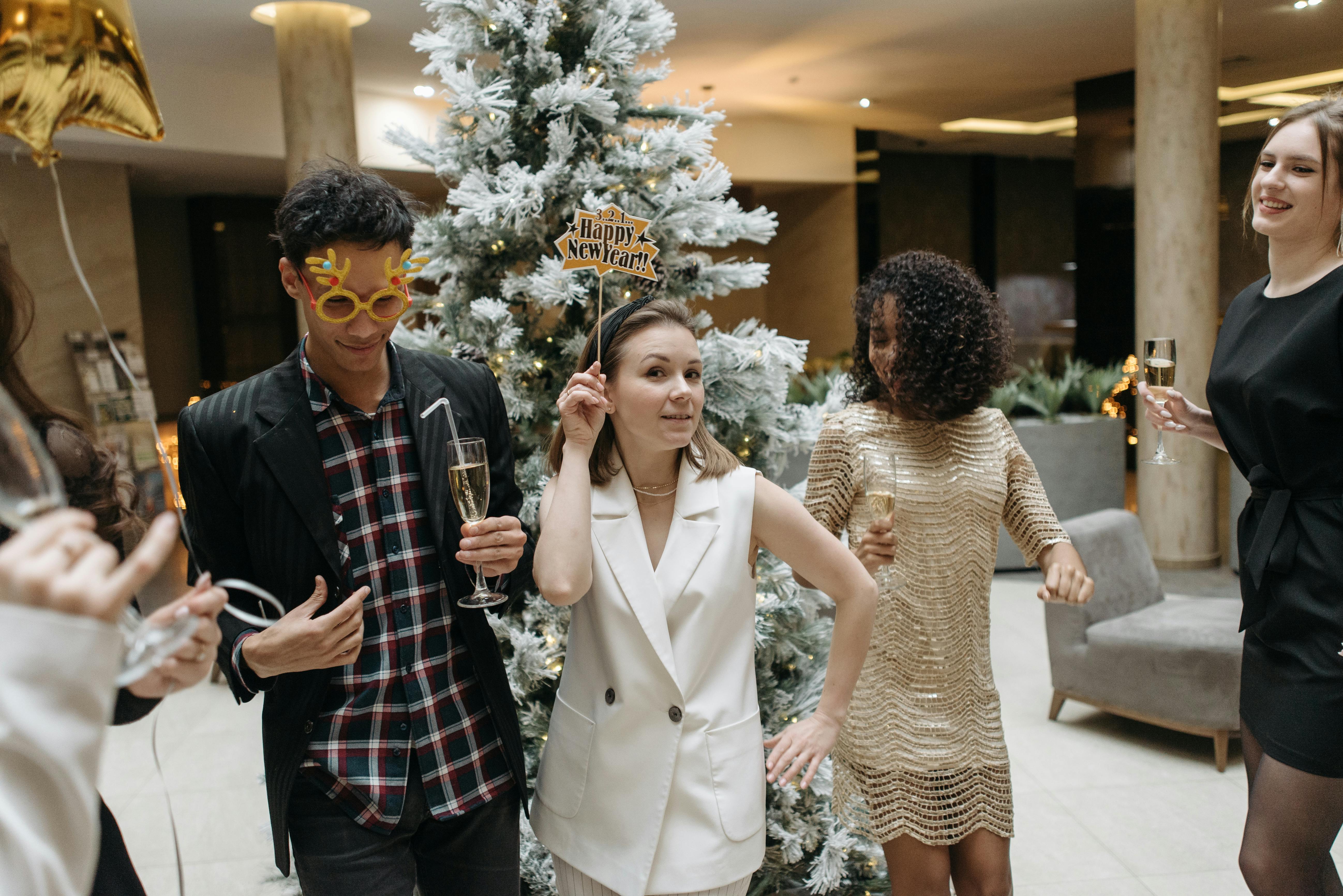 Friends celebrating New Year with drinks and decorations around a Christmas tree indoors.