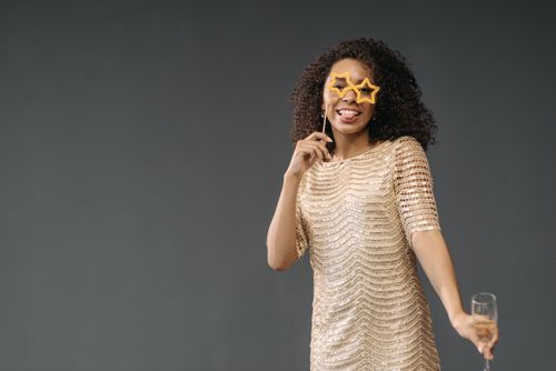 Free Happy woman posing with star-shaped glasses and a sparkly dress holding a glass of champagne. Stock Photo
